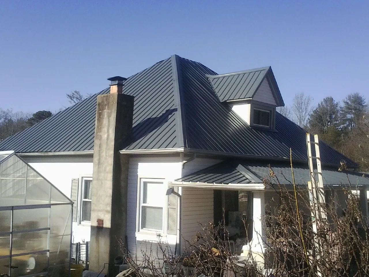 Dark blue standing seam metal roof on a white farmhouse with dormer — Slate & Tile Roof Repair by Roofing Brothers in Kamrar