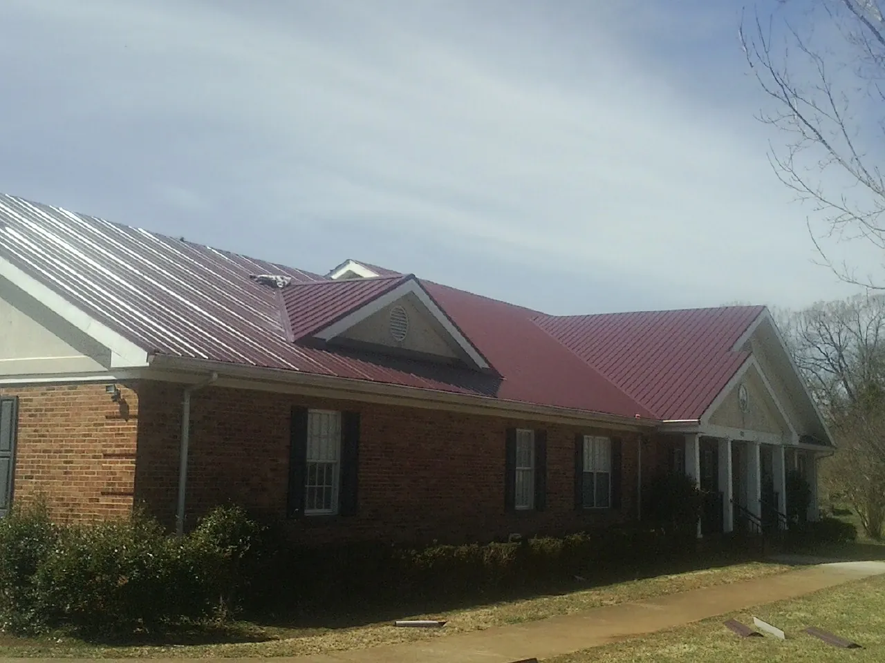 Red metal roof with gabled entries on a long brick building, from a Hail Damage Roof Repair job in Kamrar