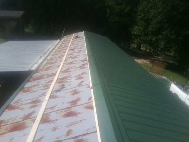 Old rusted panels beside newly installed green metal roofing — Wind Damage Roof Repair by Roofing Brothers in Kamrar