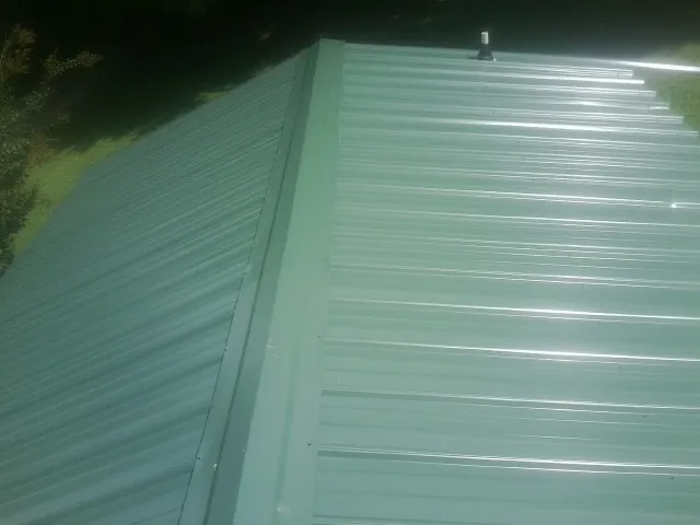 New green metal panels meeting at the ridge of a roof — Flat Roof Repair work by our crew in Kamrar