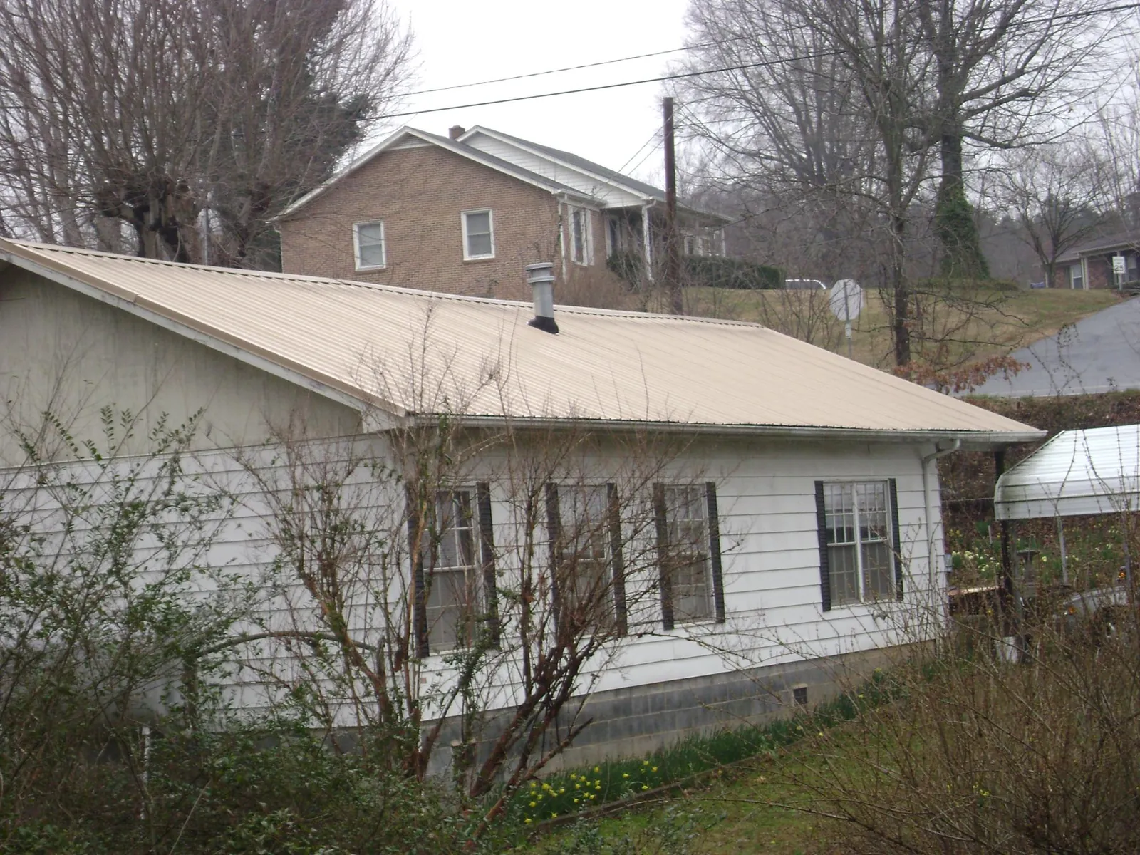 Tan metal roof on a white sided house set into a hillside — Commercial Roofing by Roofing Brothers in Kamrar