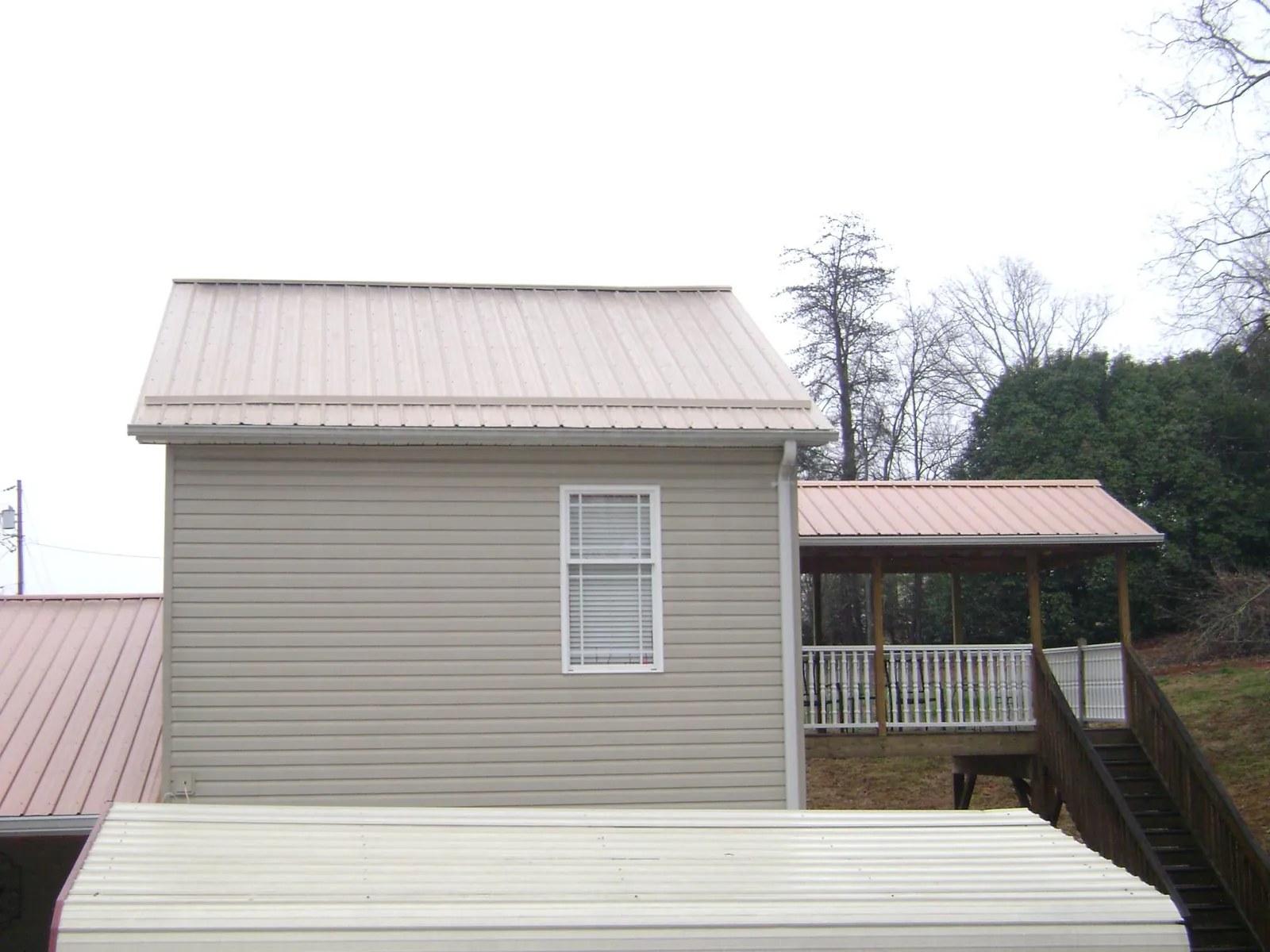 Tan metal roofs on a two story addition and attached porch, from a Roof Replacement job in Kamrar